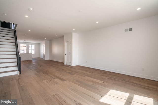 unfurnished living room with stairway, hardwood / wood-style flooring, recessed lighting, and baseboards