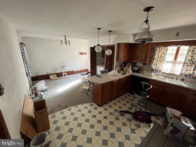kitchen featuring a sink, light countertops, washer / dryer, a peninsula, and decorative light fixtures