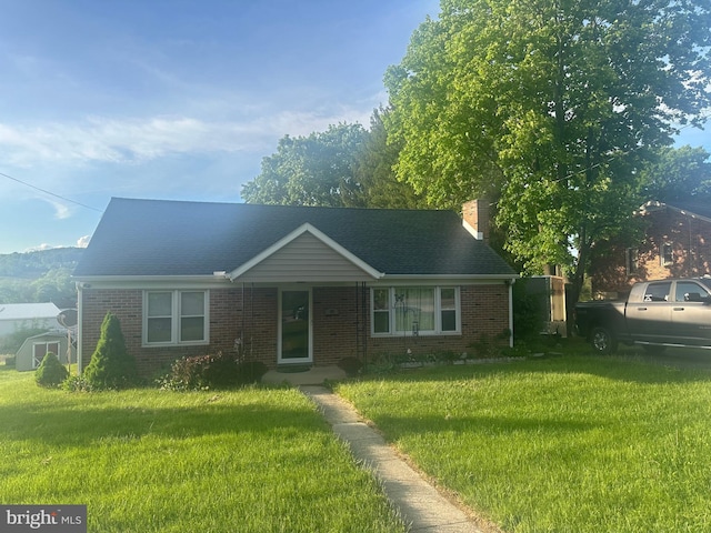 ranch-style home featuring brick siding, a front lawn, a chimney, and roof with shingles