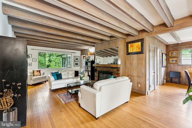 living room featuring light wood finished floors, beamed ceiling, a brick fireplace, and wood walls