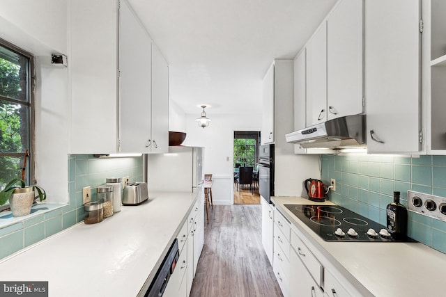 kitchen featuring under cabinet range hood, black appliances, light wood-style flooring, tasteful backsplash, and white cabinets