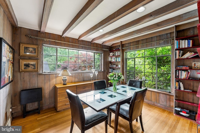 dining room with wooden walls, light wood-style flooring, and beam ceiling