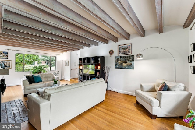 living area featuring beamed ceiling, light wood-type flooring, and baseboards