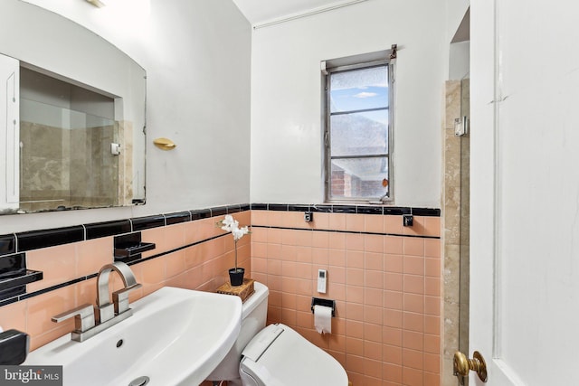 bathroom with a sink, tile walls, toilet, and a wainscoted wall