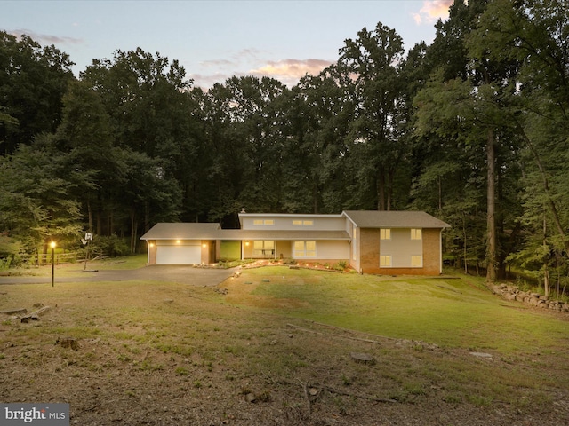 single story home with an attached garage, driveway, a front yard, and a view of trees