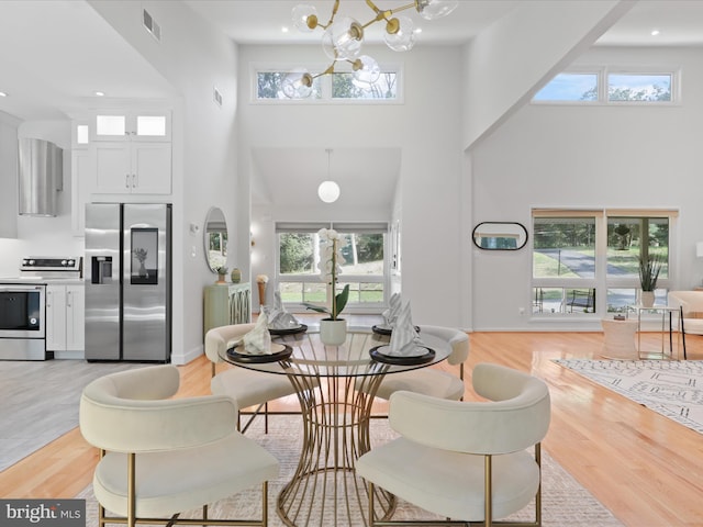dining area with a towering ceiling, light wood-style floors, and a chandelier