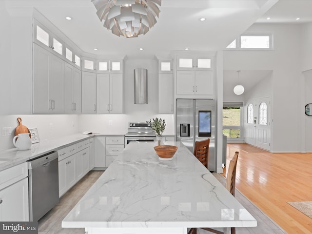 kitchen featuring stainless steel appliances, a towering ceiling, healthy amount of natural light, a center island, and white cabinetry