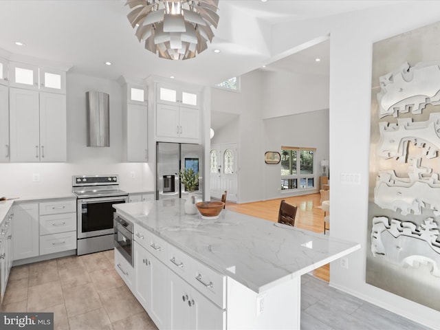 kitchen with appliances with stainless steel finishes, a center island, white cabinets, light stone countertops, and a high ceiling