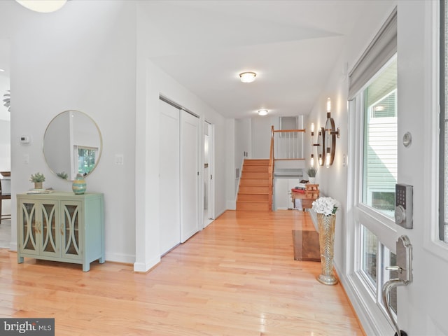 corridor featuring light wood finished floors, stairway, and baseboards
