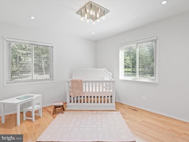 bedroom featuring wood finished floors, recessed lighting, baseboards, a nursery area, and a chandelier