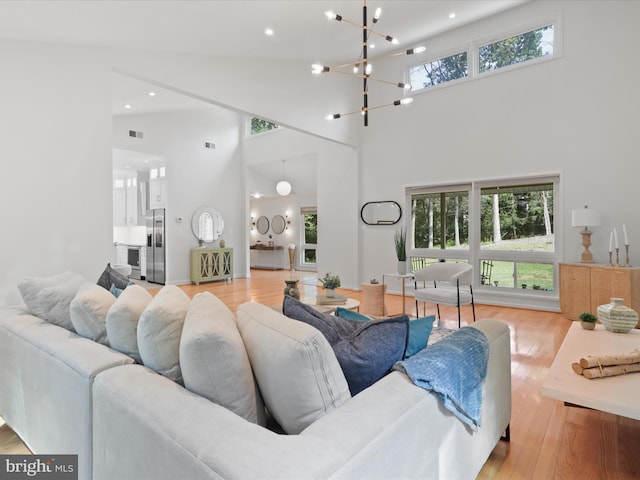 living area featuring a towering ceiling, light wood-type flooring, a chandelier, and recessed lighting