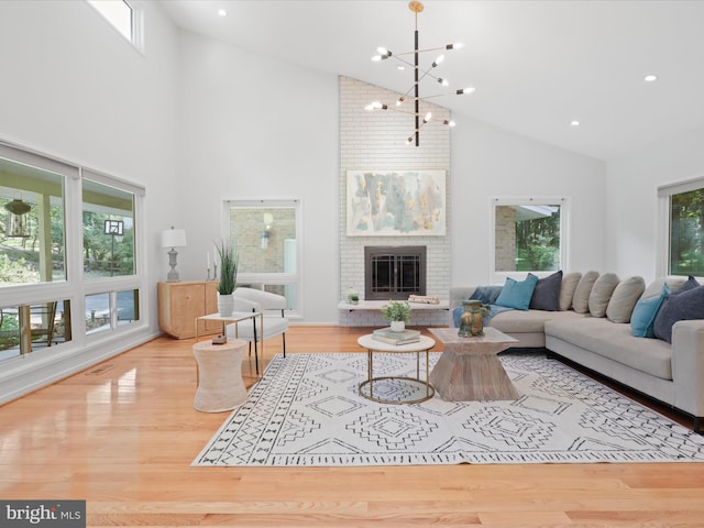 living area with high vaulted ceiling, wood finished floors, a brick fireplace, and a chandelier