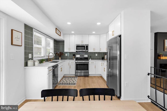 504 Kenora Dr, Millersville, MD 21108 - kitchen featuring appliances with stainless steel finishes, a sink, light wood-style floors, tasteful backsplash, and white cabinetry