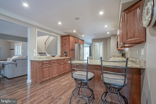 kitchen with freestanding refrigerator, light wood-style flooring, a sink, recessed lighting, and brown cabinetry