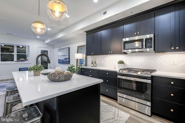 426 Manor Pl NW Unit 1, Washington, DC 20010 - kitchen with stainless steel appliances, light countertops, light wood-type flooring, a breakfast bar area, and decorative backsplash