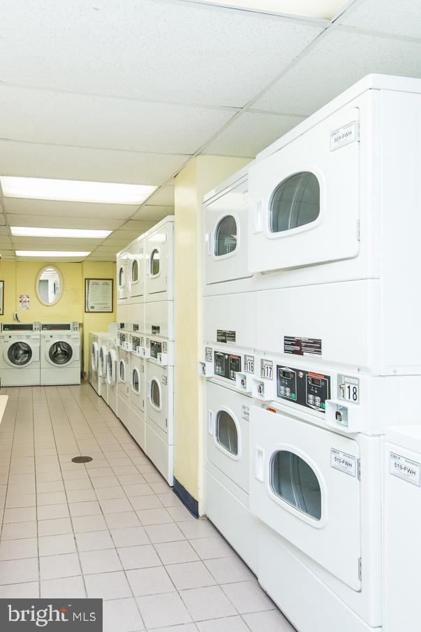 shared laundry with estacked washer and dryer, washer and clothes dryer, and light tile patterned floors