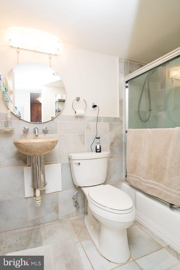 full bath featuring toilet, bath / shower combo with glass door, tile walls, and a sink