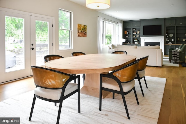 dining room featuring healthy amount of natural light, light wood-style floors, a fireplace, and french doors