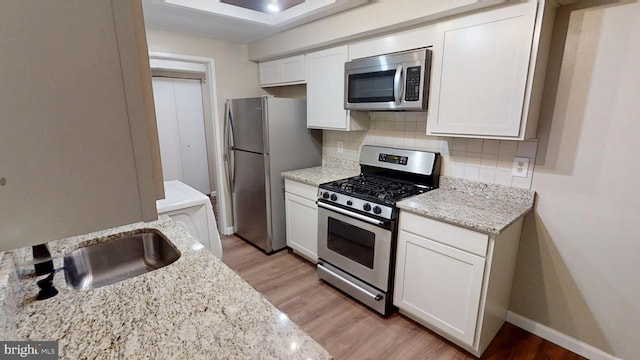 10239 Prince Pl Unit 26-T1, Upper Marlboro, MD 20774 - kitchen with appliances with stainless steel finishes, decorative backsplash, a sink, white cabinetry, and light wood-style floors