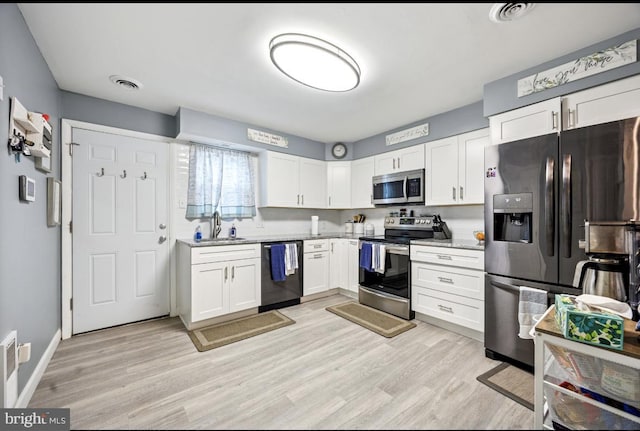 kitchen featuring stainless steel appliances, white cabinets, light wood-type flooring, a sink, and light stone counters