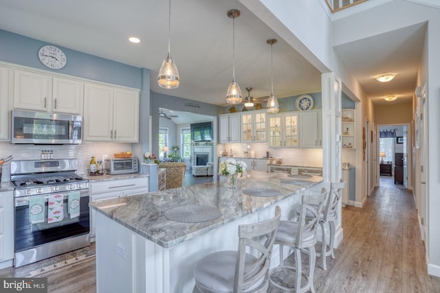 kitchen with appliances with stainless steel finishes, a ceiling fan, white cabinets, tasteful backsplash, and light stone countertops
