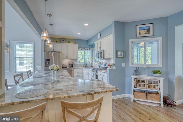 kitchen with appliances with stainless steel finishes, light wood-style flooring, white cabinetry, a kitchen bar, and recessed lighting
