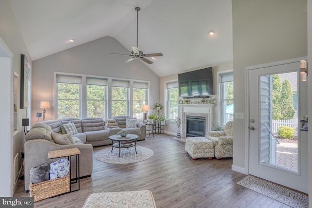 living area with high vaulted ceiling, a ceiling fan, a fireplace with flush hearth, wood finished floors, and baseboards