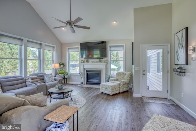 living area with high vaulted ceiling, ceiling fan, baseboards, a fireplace with flush hearth, and wood-type flooring