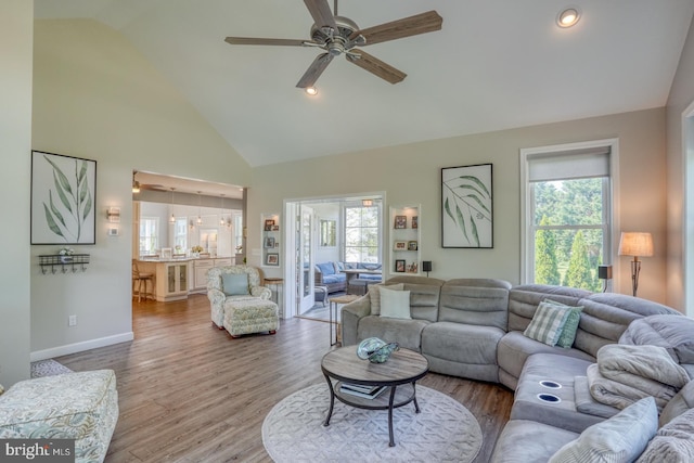 living area with a ceiling fan, high vaulted ceiling, wood finished floors, and baseboards