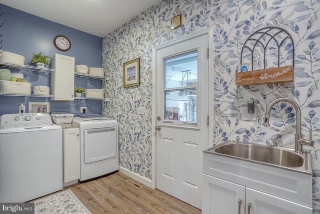 clothes washing area with wallpapered walls, washing machine and clothes dryer, cabinet space, light wood-type flooring, and baseboards