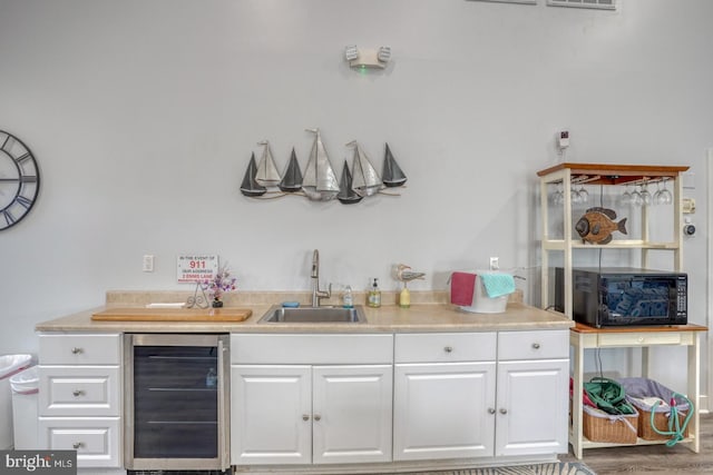 bar area featuring beverage cooler, a sink, black microwave, and wood finished floors
