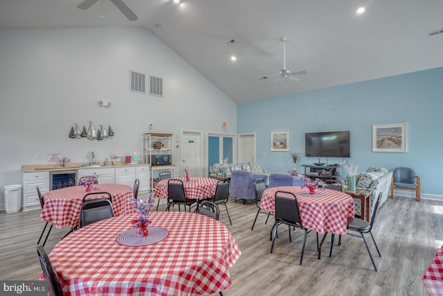 dining room with ceiling fan, high vaulted ceiling, beverage cooler, light wood-style floors, and baseboards
