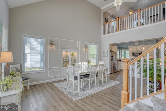 dining area with a towering ceiling, a ceiling fan, stairway, and light wood-style floors