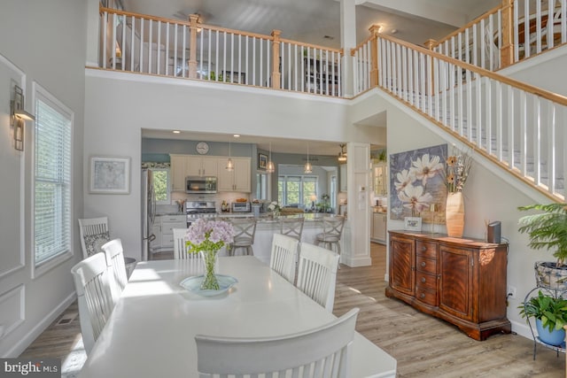dining room with light wood-style flooring, a high ceiling, baseboards, and stairway