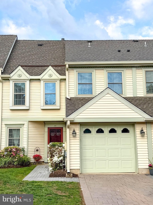 townhome / multi-family property featuring decorative driveway, a garage, and roof with shingles