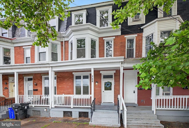view of property featuring covered porch, brick siding, and mansard roof