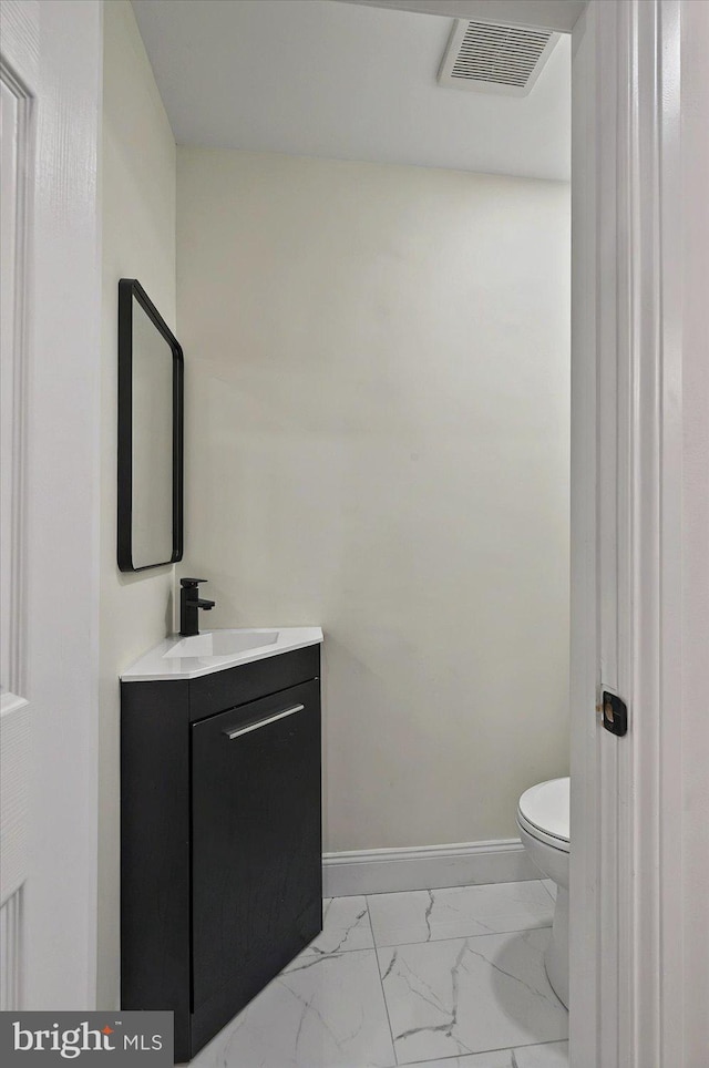 half bathroom featuring marble finish floors, vanity, toilet, and baseboards