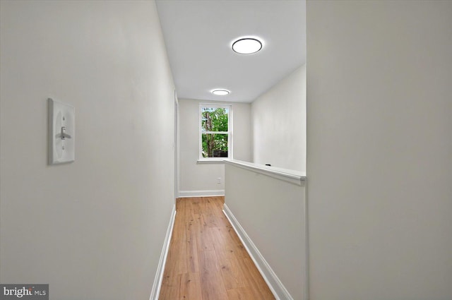 corridor featuring light wood finished floors, baseboards, and an upstairs landing
