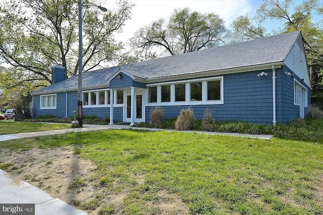 ranch-style house with a chimney, a front lawn, and roof with shingles