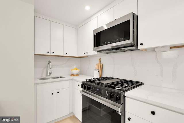 kitchen with gas stove, stainless steel microwave, a sink, backsplash, and white cabinets
