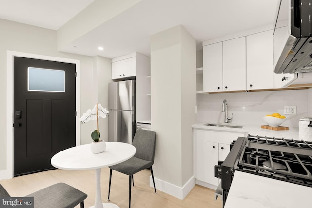 kitchen featuring a sink, freestanding refrigerator, tasteful backsplash, light countertops, and white cabinetry