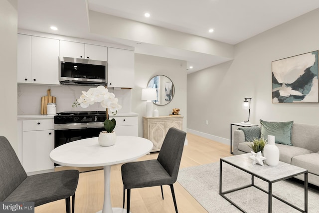 kitchen featuring stainless steel microwave, light wood finished floors, white cabinetry, baseboards, and stove