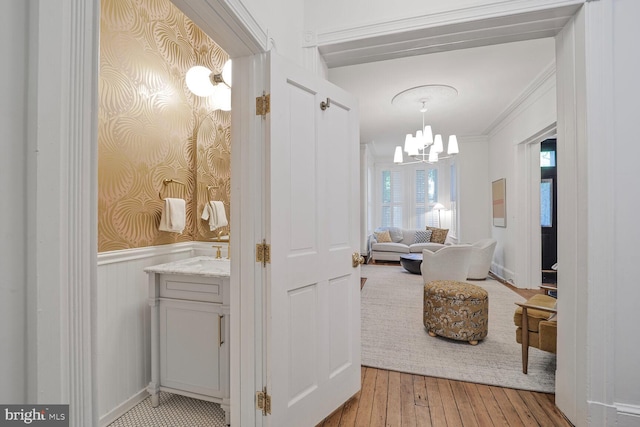 hallway with a wainscoted wall, a chandelier, light wood-style floors, wallpapered walls, and crown molding