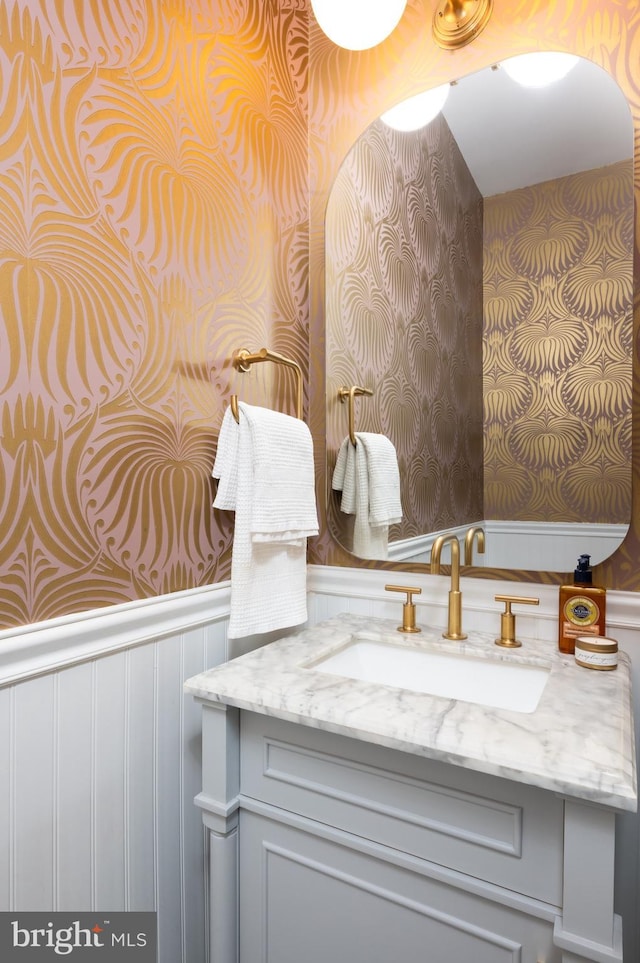 bathroom featuring wallpapered walls, wainscoting, vanity, and a decorative wall