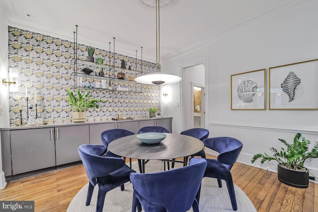 dining area with wood-type flooring, ornamental molding, and an accent wall