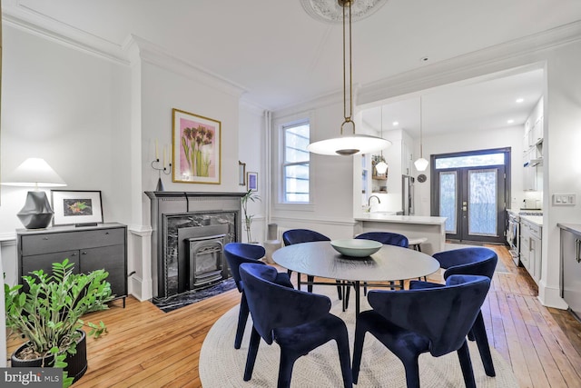 dining room with a premium fireplace, ornamental molding, and light wood-type flooring