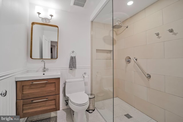 bathroom with tiled shower, vanity, toilet, a wainscoted wall, and tile patterned flooring