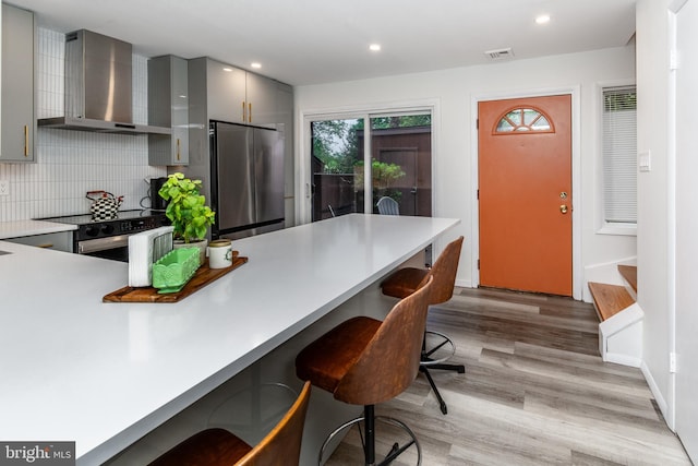23 Eden Roc, New Hope, PA 18938 - kitchen featuring stainless steel refrigerator, wall chimney exhaust hood, gray cabinets, a breakfast bar, and light wood-style flooring