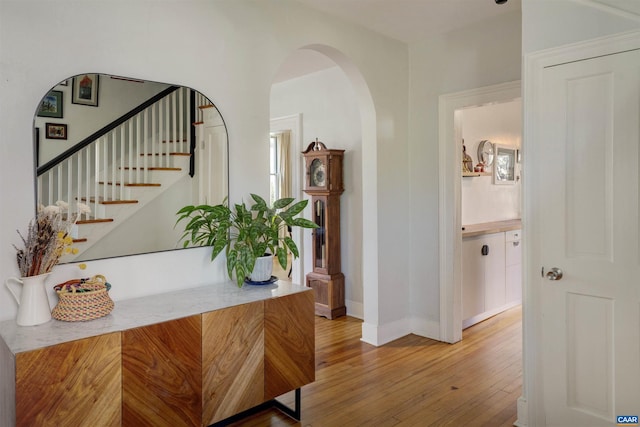 hall featuring hardwood / wood-style flooring, arched walkways, baseboards, and stairway