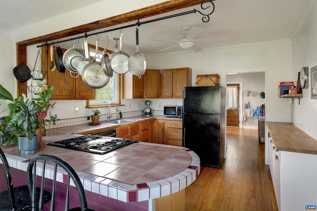 kitchen with freestanding refrigerator, stainless steel microwave, a sink, tile counters, and cooktop